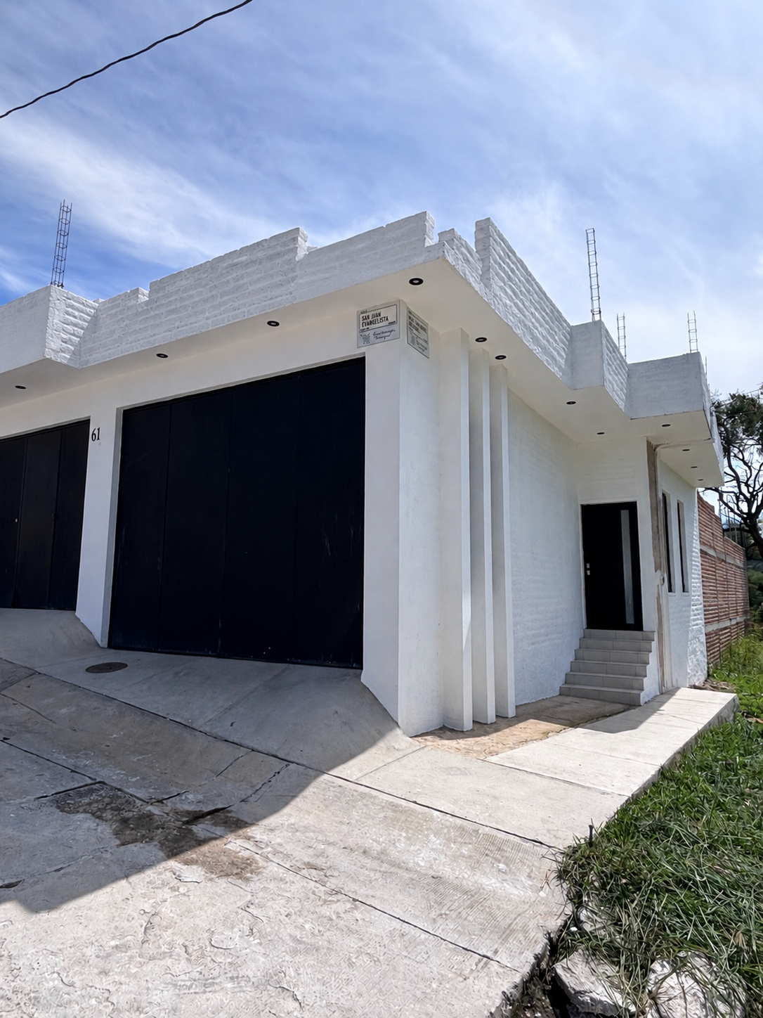 Fachada exterior blanca de Luciérnaga terraza con portones negros y acceso principal